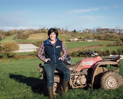 An image of a women with dark hair sat on the front of a quad bike, set against a farming landscape with a blue sky.